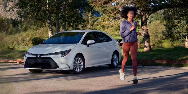 White 2024 Toyota Corolla and its owner jogging away from it.