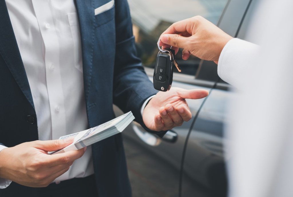 A car salesman exchanging keys for cash with a customer.