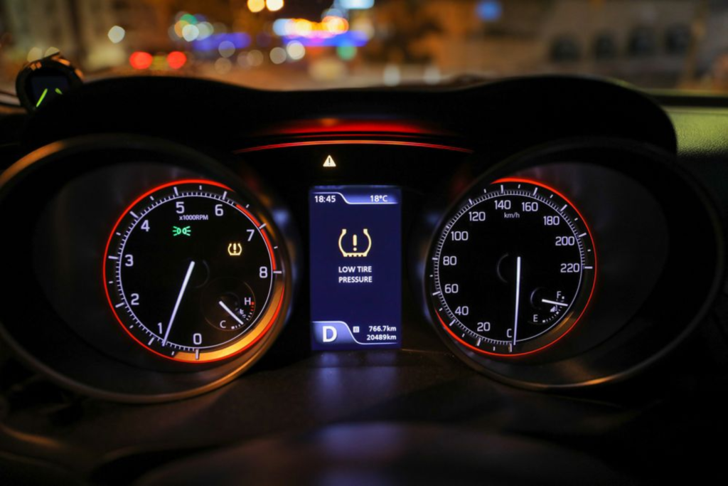 The image shows a car dashboard with a low tire pressure warning displayed on the screen.